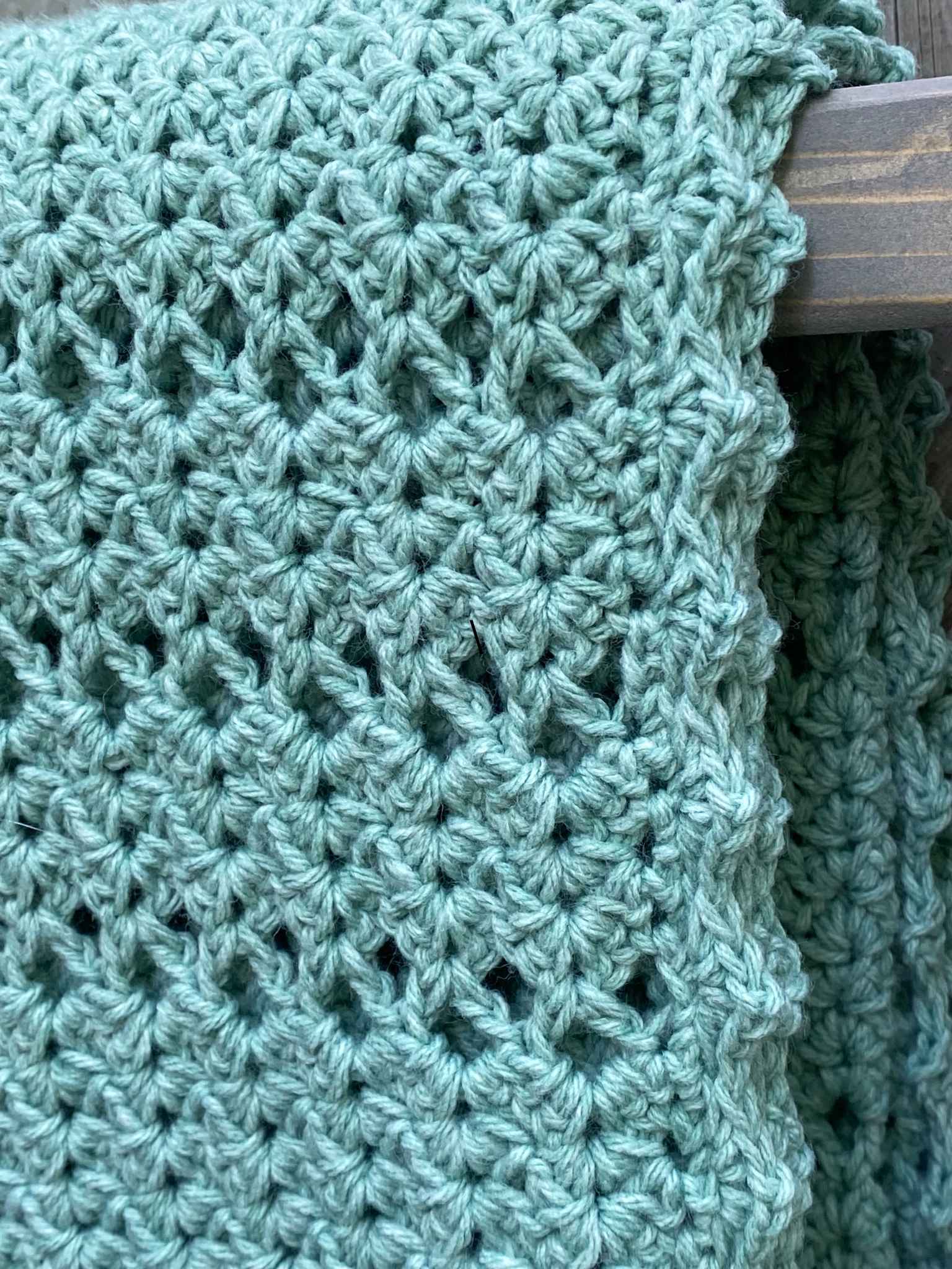 a light greenish blanket that is crocheted and hanging on a blanket ladder